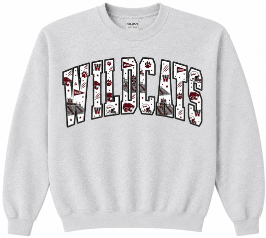 A light gray crewneck sweatshirt featuring a large 'WILDCATS' graphic across the chest. The letters are filled with various wildcat-themed illustrations, including paw prints, flags, and a cat statue, outlined in black.